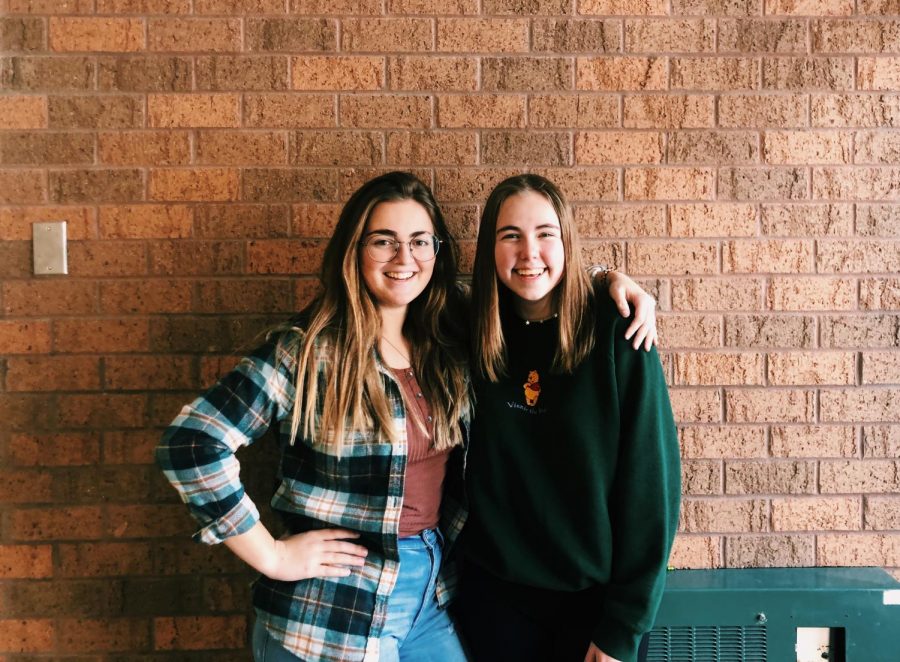 The new Table Toppers club ambassadors seniors Elle Ohlman and Dana Kistler pose in front of a brick wall.