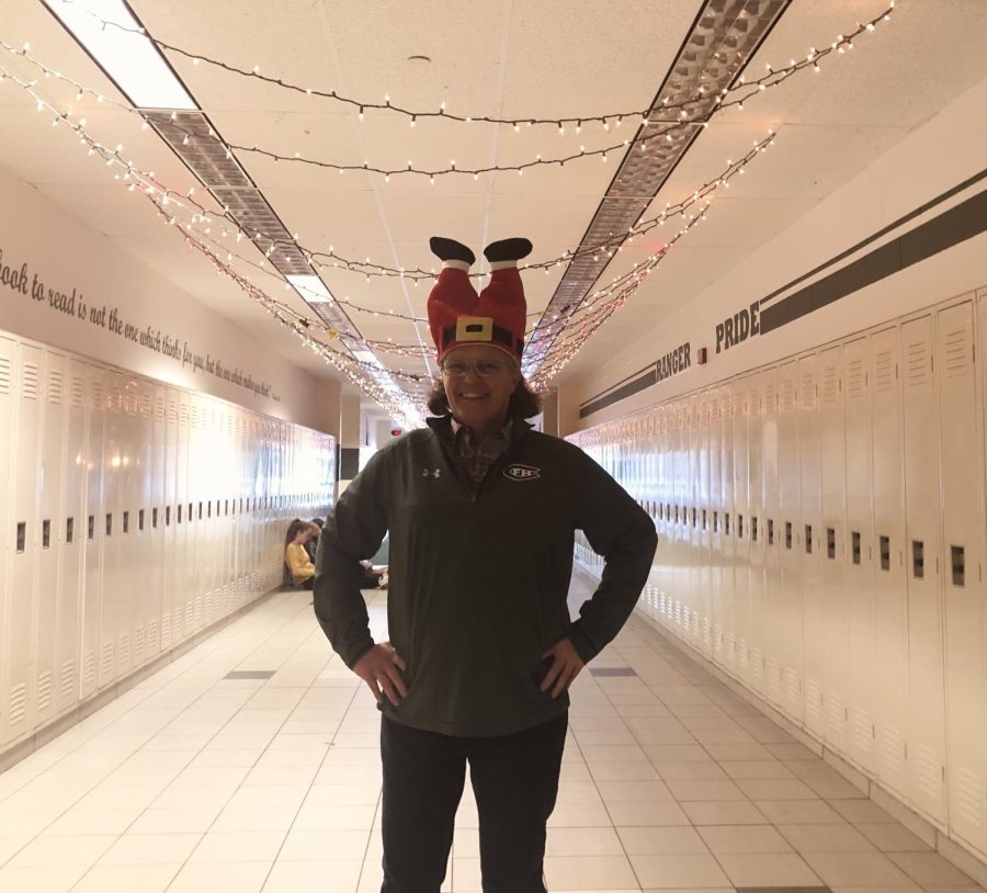 Mrs. Stiles standing with her Christmas hat in front of the hallway lights 