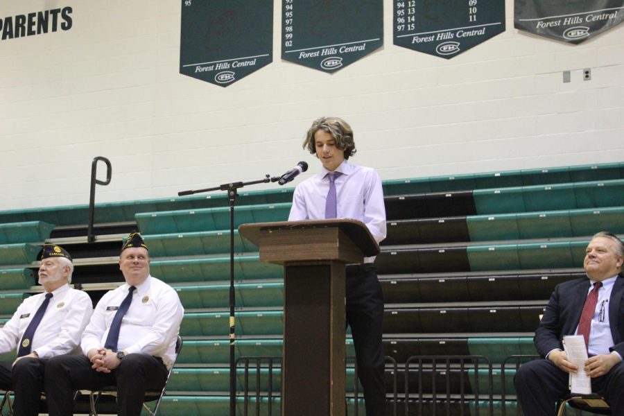 Charlie reading his poem aloud to the gymnasium as veterans, students, and staff listen attentively.
