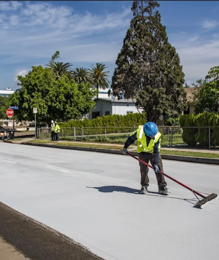 Road construction workers applying the light-colored sealant on city streets. 