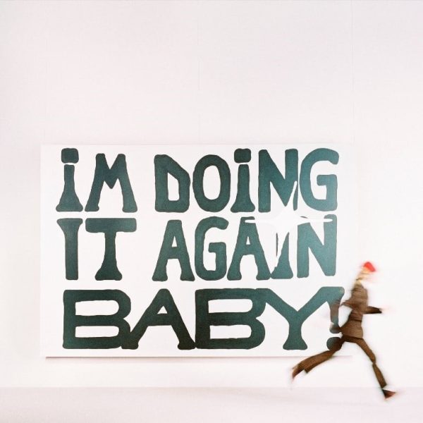 Girl in reds 2024 album cover for IM DOING IT AGAIN BABY!, depicting her running in front of a sign advertising the release. 